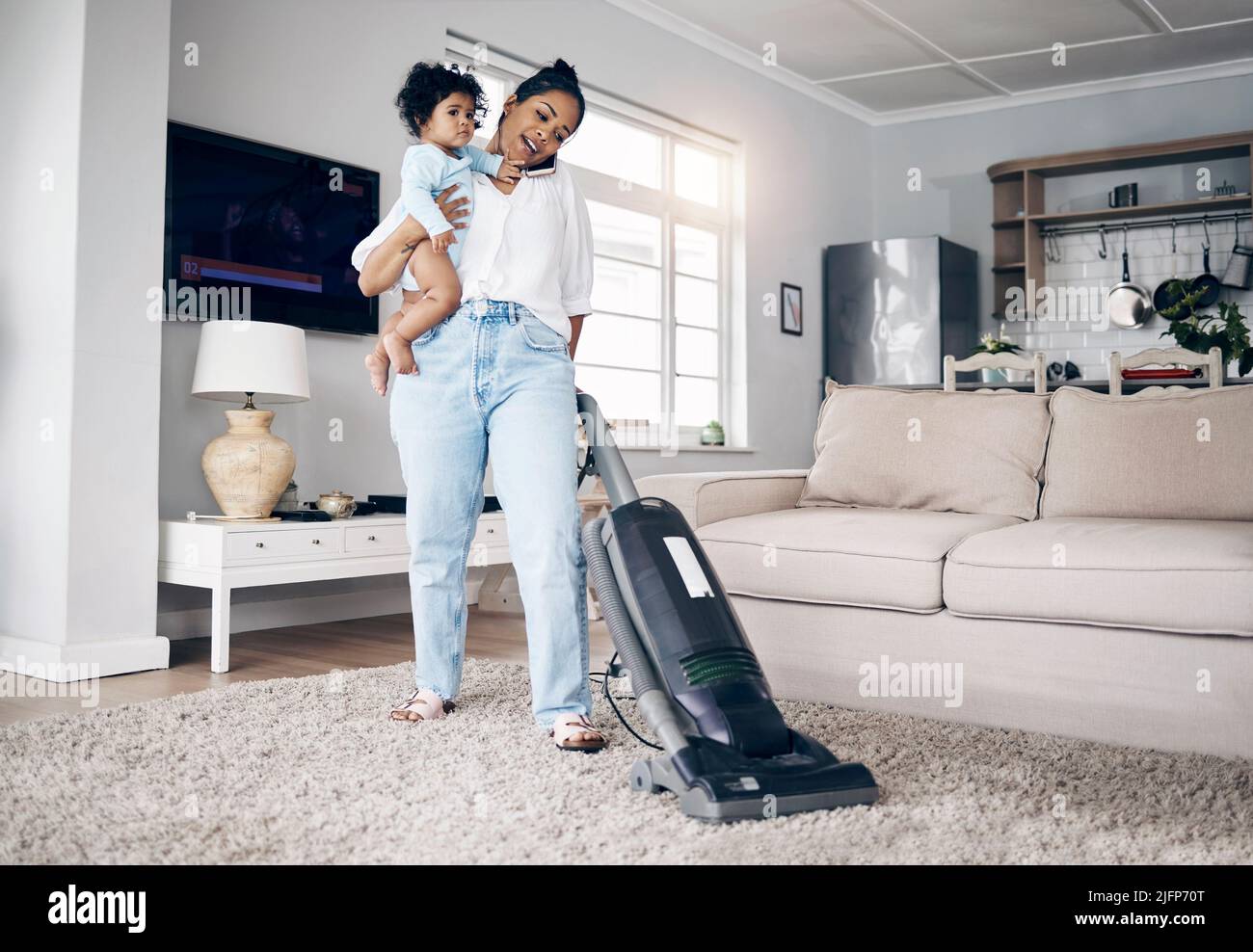 She does it all. Shot of a young mother using a cellphone while completing housework and holding her baby at home. Stock Photo