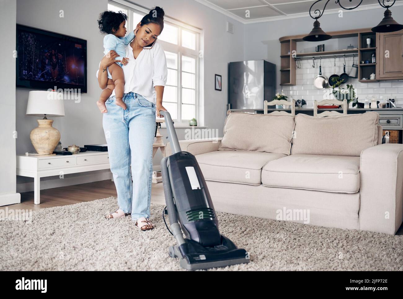 Her mind is skilfully in different places. Shot of a young mother using a cellphone while completing housework and holding her baby at home. Stock Photo