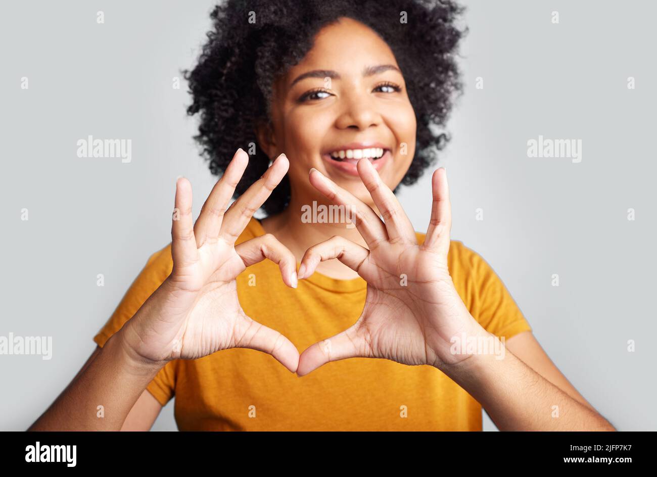 Put some love into it. Shot of a young woman forming a heart shape while posing against a grey background. Stock Photo