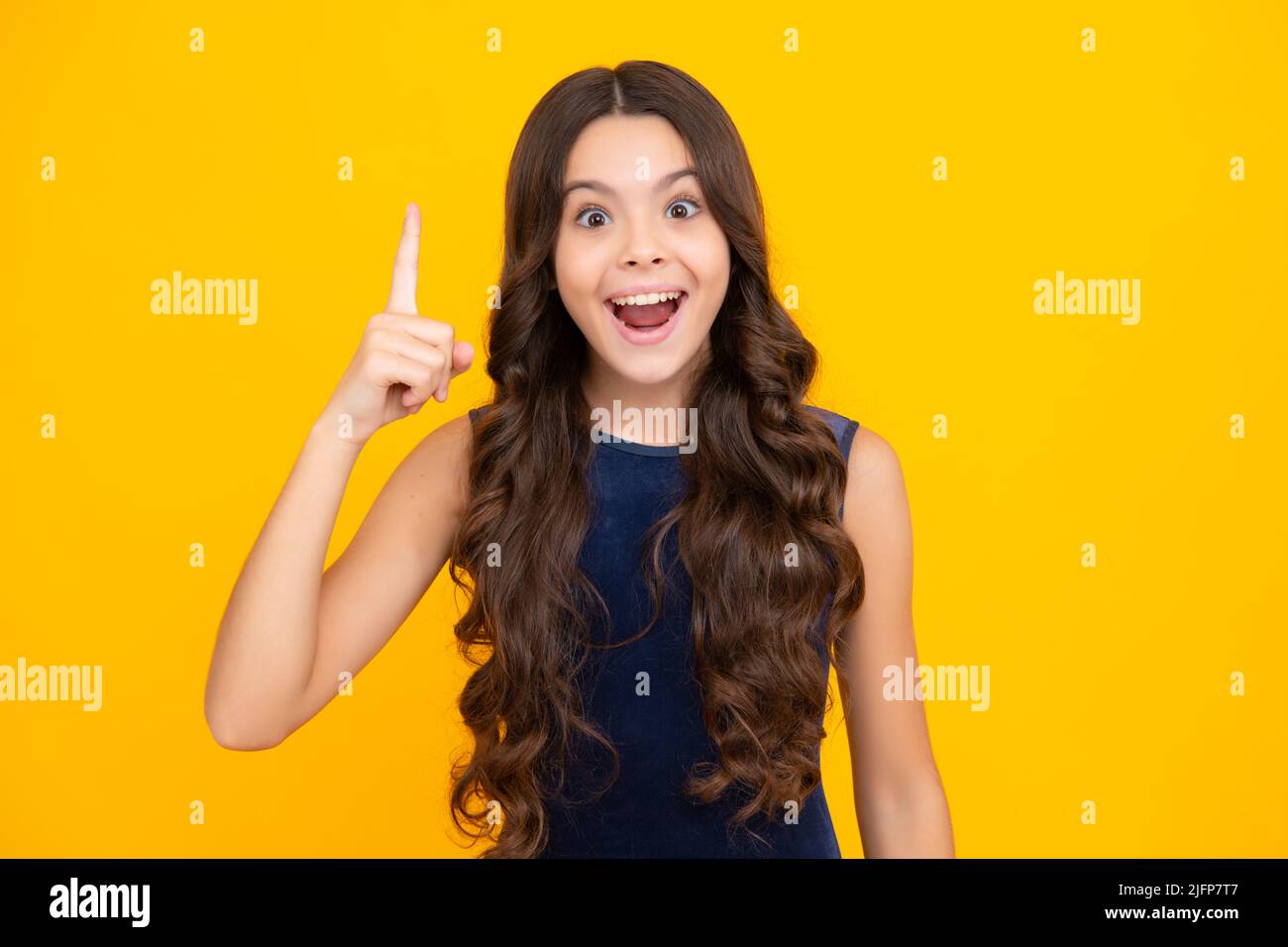 Excited face, cheerful emotions of teenager girl. Portrait of young teenager pointing up with finger, isolated on yellow background. Funny school girl Stock Photo