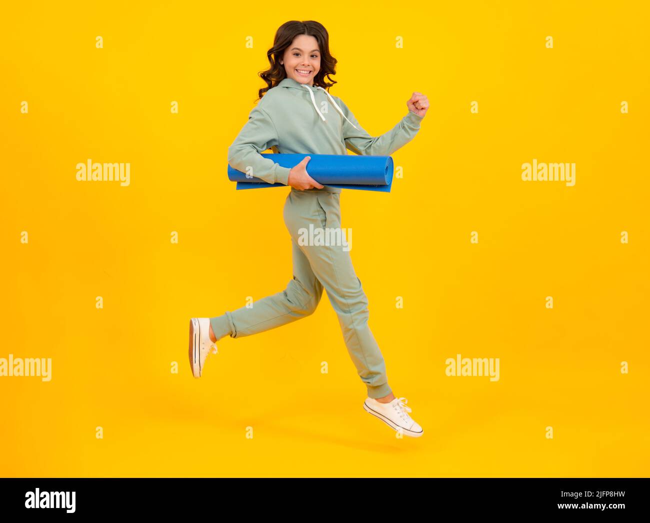 Sportswear advertising concept. Run and jump. Teenager child girl in tracksuits jogging suit posing in the studio hold fitness mat. Stock Photo