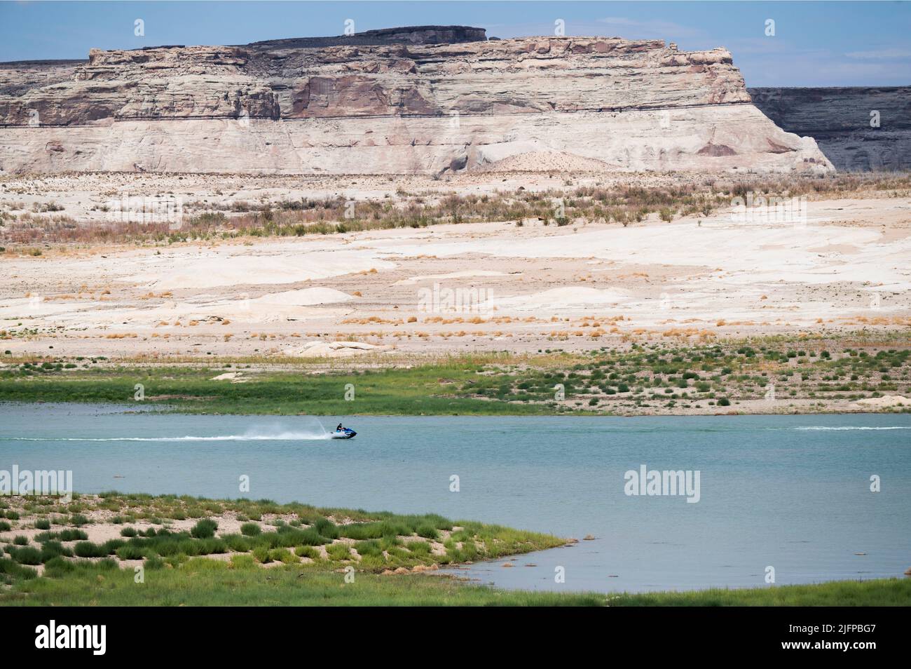 June 30, 2022 - Glen Canyon National Recreation Area, Utah, U.S. - A person rides his personal watercraft near an area of Lake Powell that used to be underwater that is now nearly dry at Lone Rock Beach on June 30, 2022 in Big Water, Utah. As severe drought grips parts of the Western United States, water levels at Lake Powell have dropped to their lowest levels since the lake was created by damming the Colorado River in 1963. The Colorado River Basin connects Lake Powell and Lake Mead and supplies water to 40 million people in seven western states. (Credit Image: © David Becker/ZUMA Press Wire Stock Photo