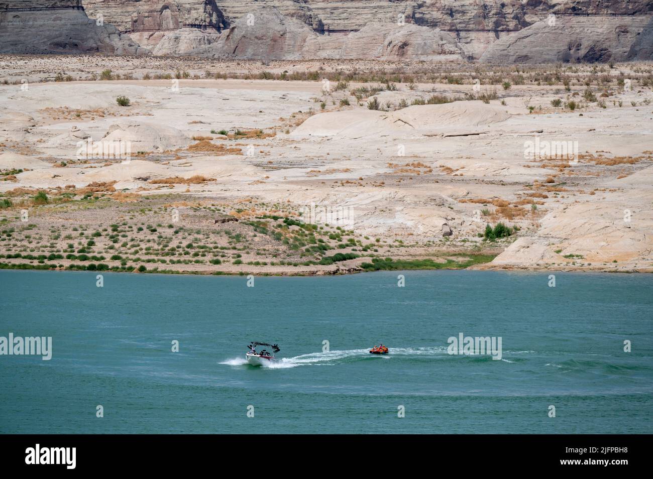 June 30, 2022 - Glen Canyon National Recreation Area, Utah, U.S. - Boaters ride near an area of Lake Powell that used to be underwater that is now nearly dry at Lone Rock Beach on June 30, 2022 in Big Water, Utah. As severe drought grips parts of the Western United States, water levels at Lake Powell have dropped to their lowest levels since the lake was created by damming the Colorado River in 1963. The Colorado River Basin connects Lake Powell and Lake Mead and supplies water to 40 million people in seven western states. (Credit Image: © David Becker/ZUMA Press Wire) Stock Photo