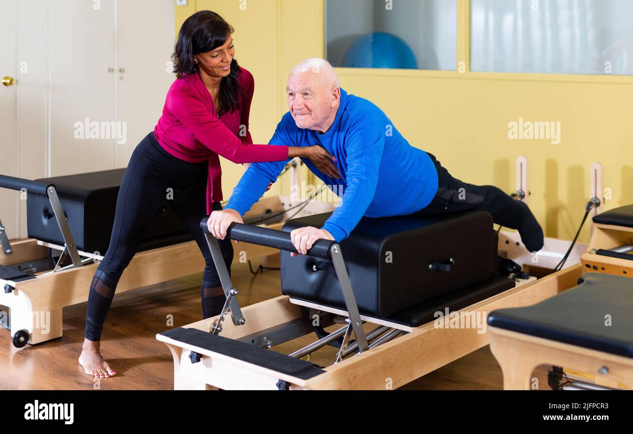 Elderly man practicing pilates on reformer under supervision of