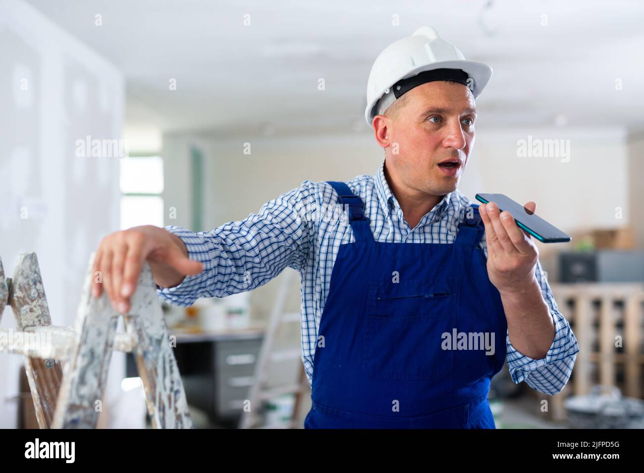 Foreman using smartphone, recording voice message Stock Photo