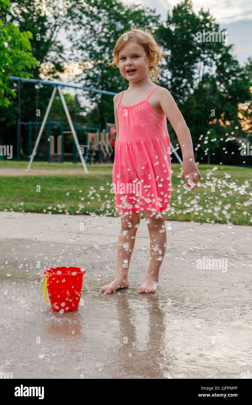 Little girl standing at water park playground. Child playing near fountain in summer outdoors Stock Photo