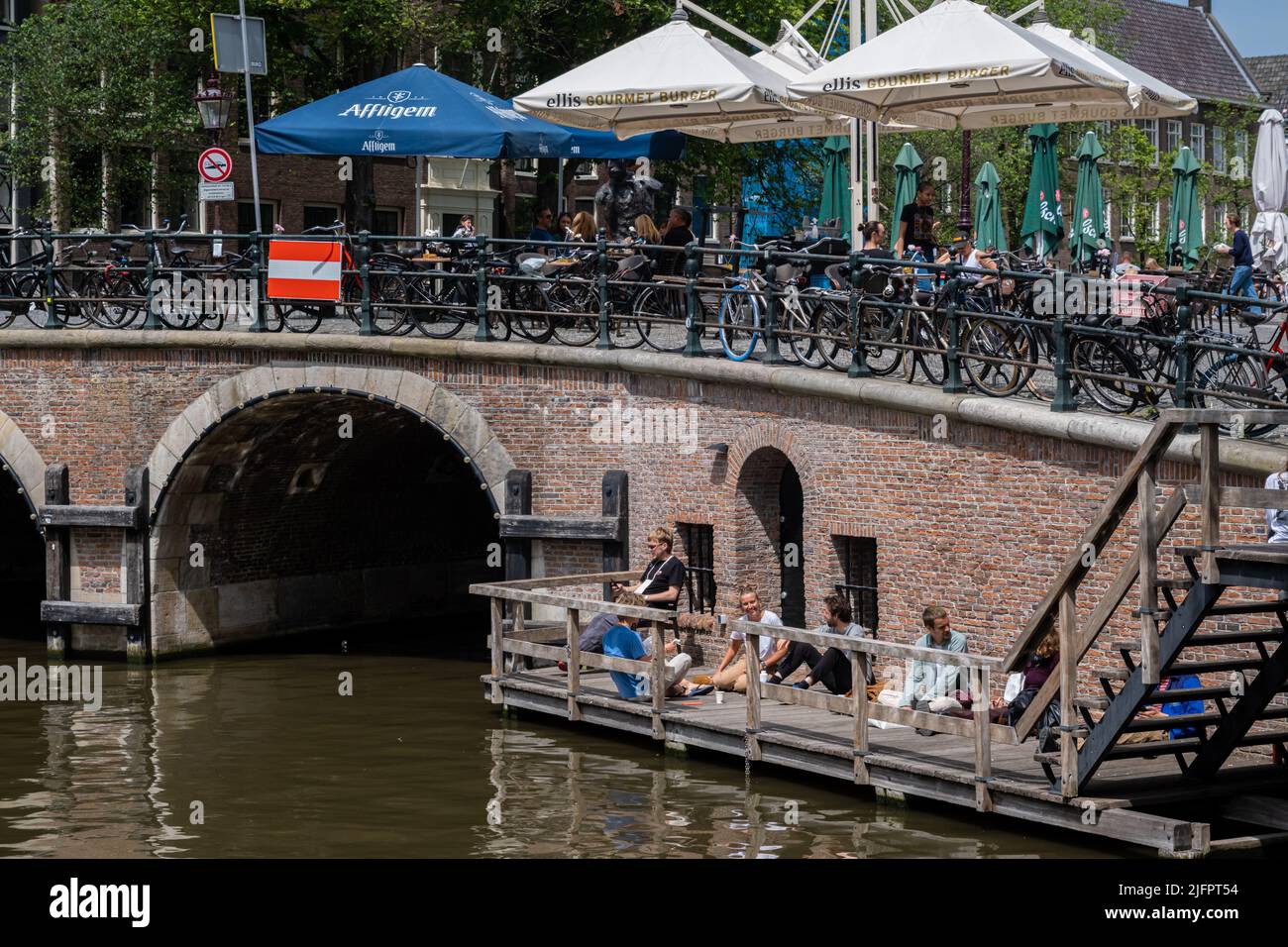 Amsterdam, The Netherlands - 21 June 2022: Old bridge in central Amsterdam with people sitting by the water Stock Photo