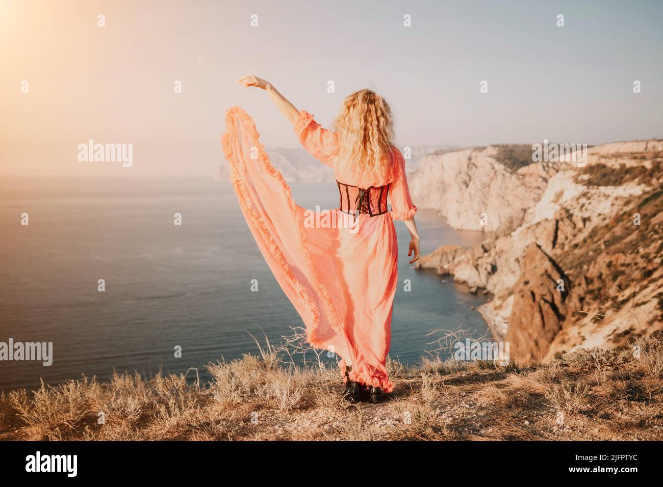 Beautiful young caucasian woman with curly blond hair and freckles. Cute redhead woman portrait in a pink long dress posing on a volcanic rock high Stock Photo