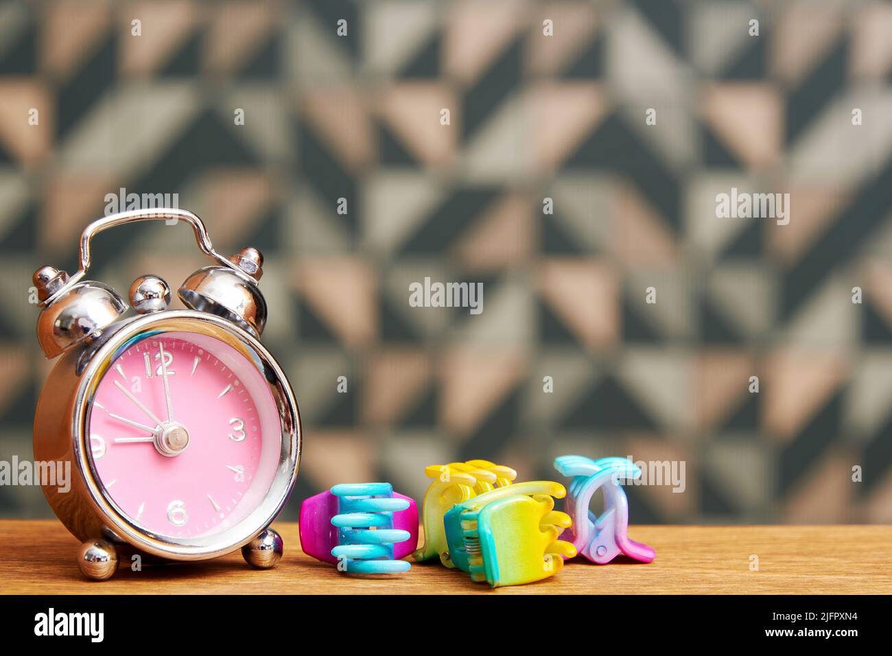 Small fancy alarm clock and colorful hairpins on the wooden bed table