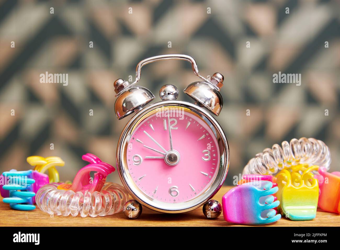 Pink fancy alarm clock with girly hairpins on the bed table. Teenage