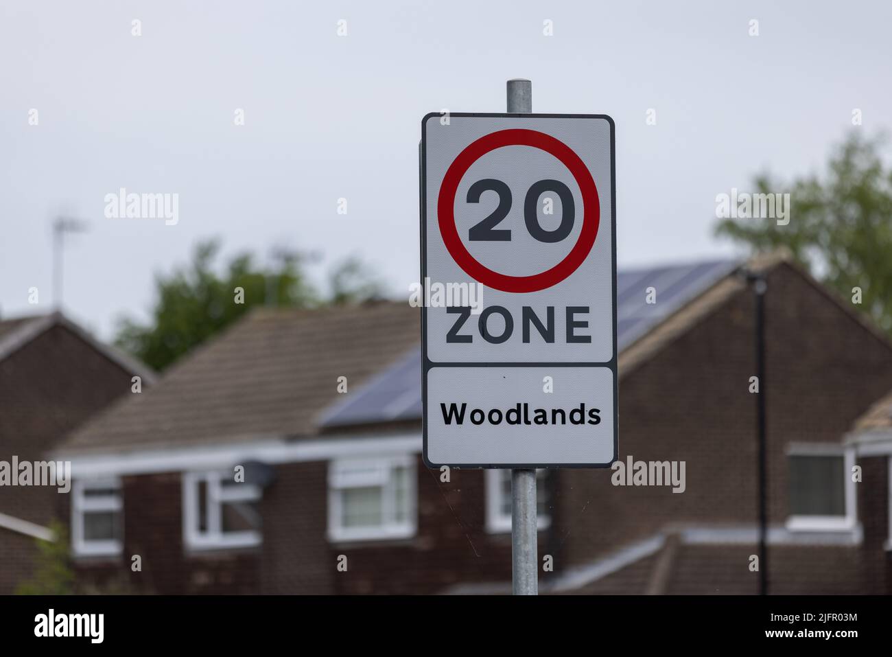 Public speed limit sign at urban area in Harrogate, UK saying 20 zone Woodlands with houses in the background Stock Photo