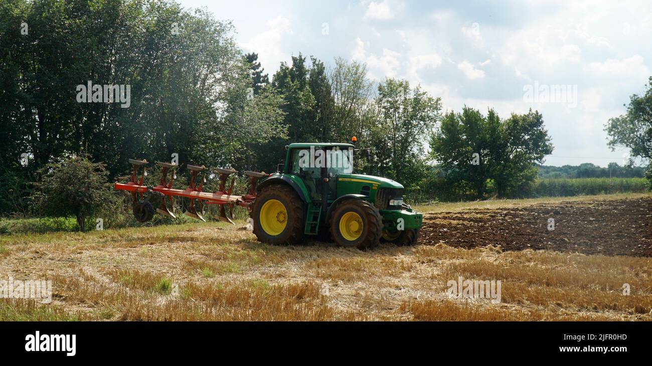 Green John Deere Tractor ploughing in stubble. Stock Photo