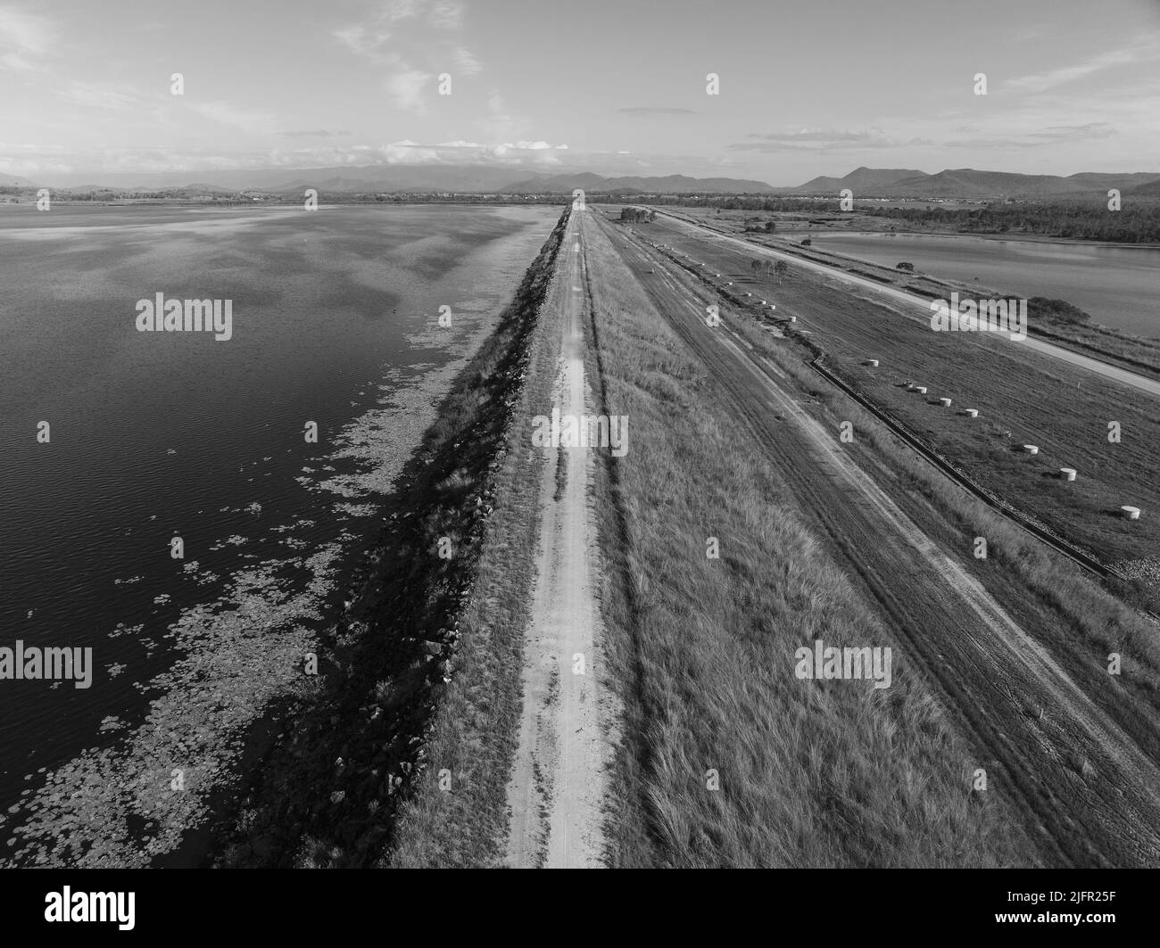 Droning along a dam wall with aquatic plants edging the water and a pond containment on the