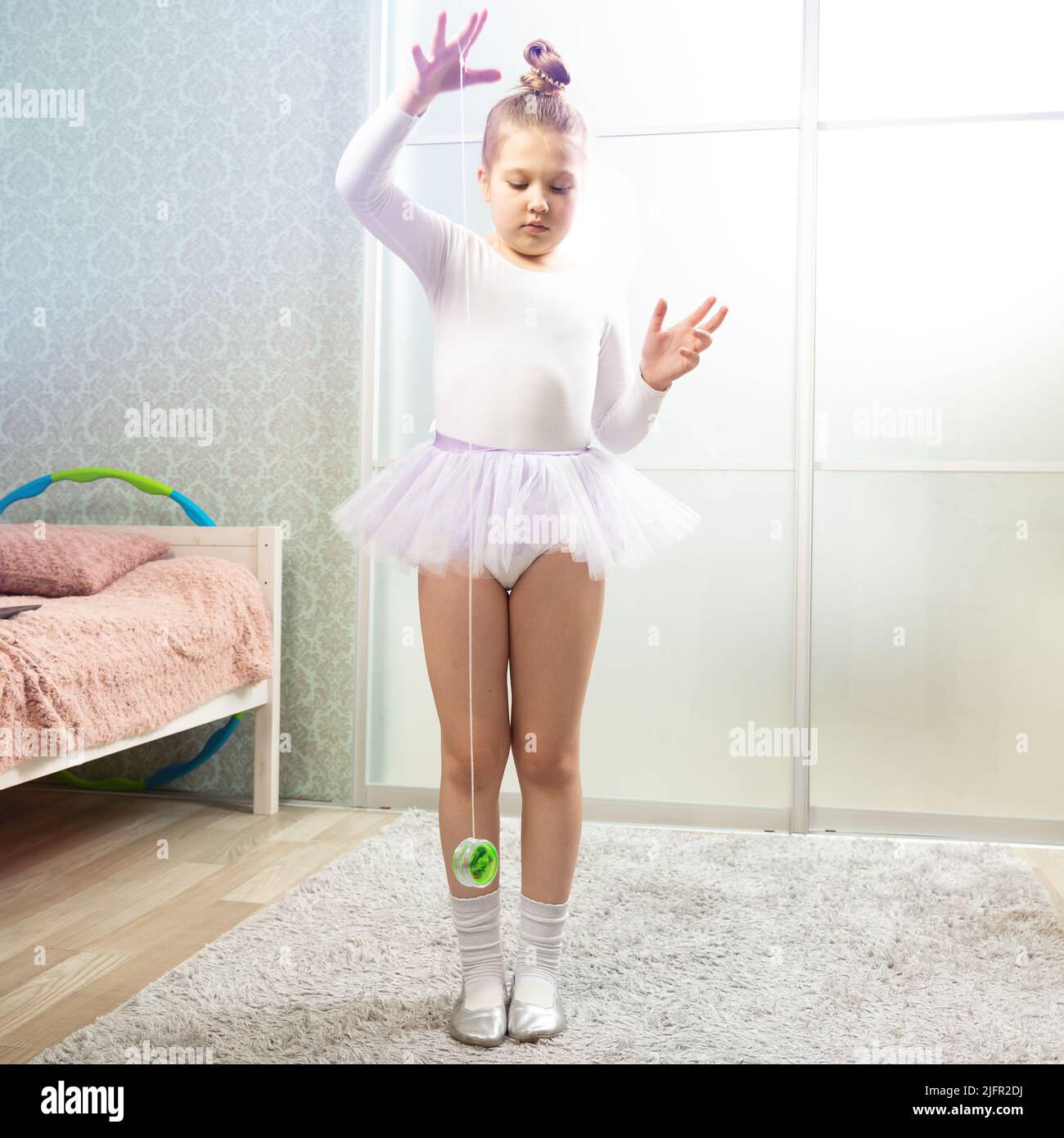 A little ballerina in a white swimsuit dances at home, learns to dance and plays yo-yo. Dance lessons at home. Stock Photo