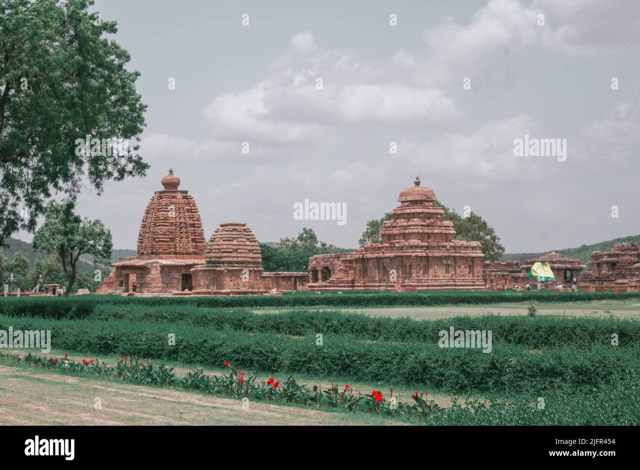 A view of the Pattadakal surrounded by hedges with a cloudy sky in the background Stock Photo