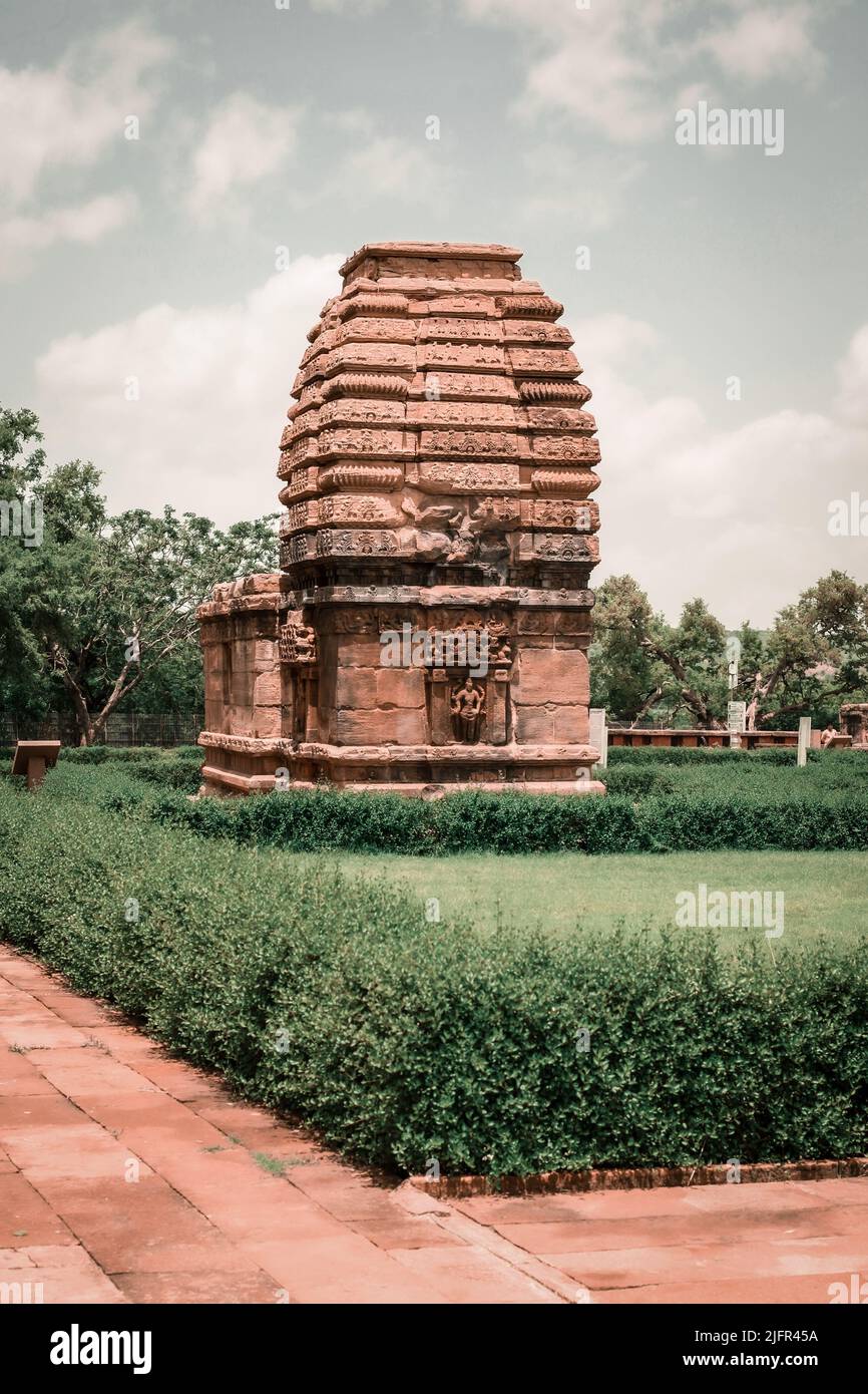 A vertical shot of a structure in Pattadakal surrounded by hedges with a cloudy sky in the background Stock Photo