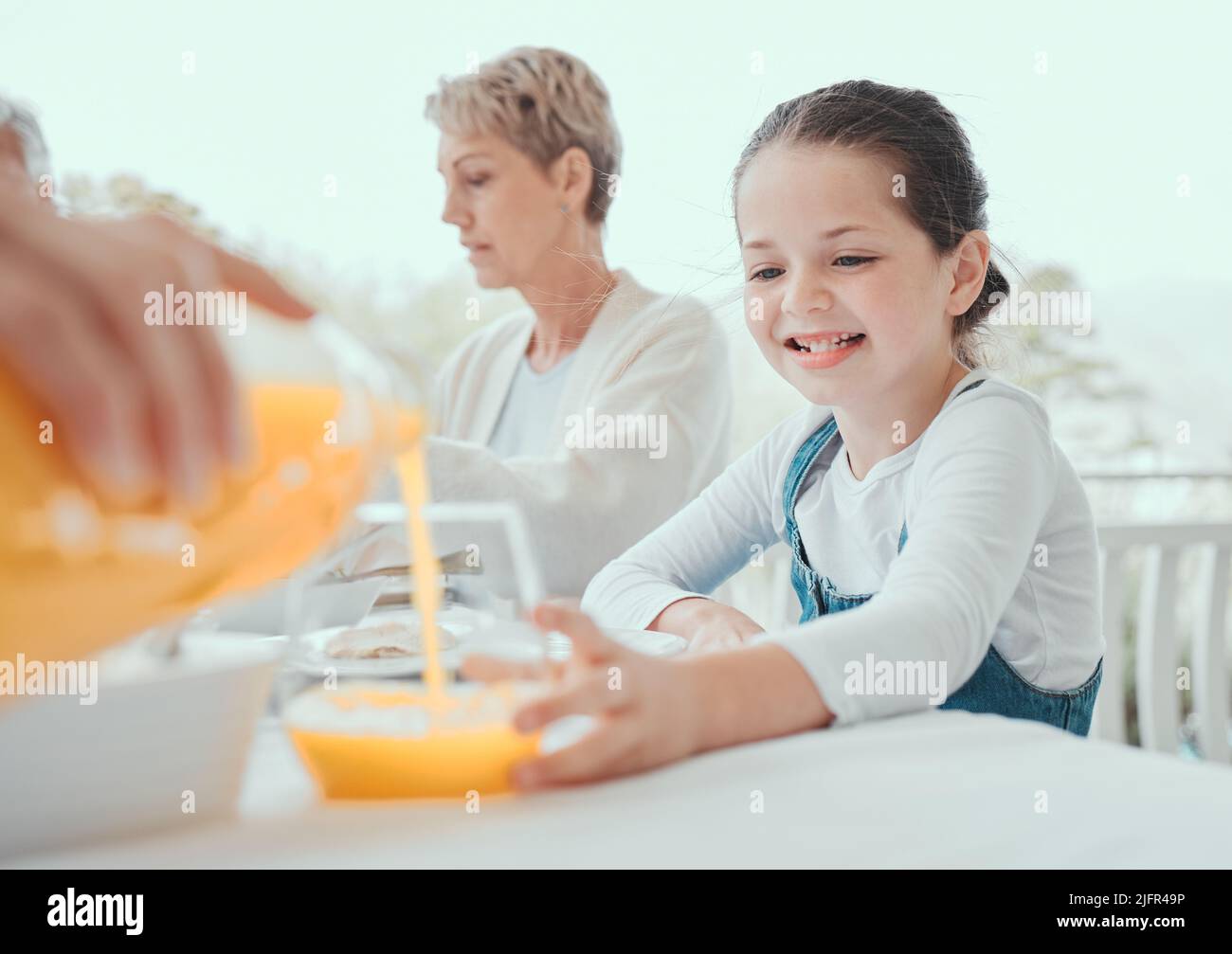 Home is the body, the table is the heart. Shot of a little girl getting some juice from a family member at home. Stock Photo