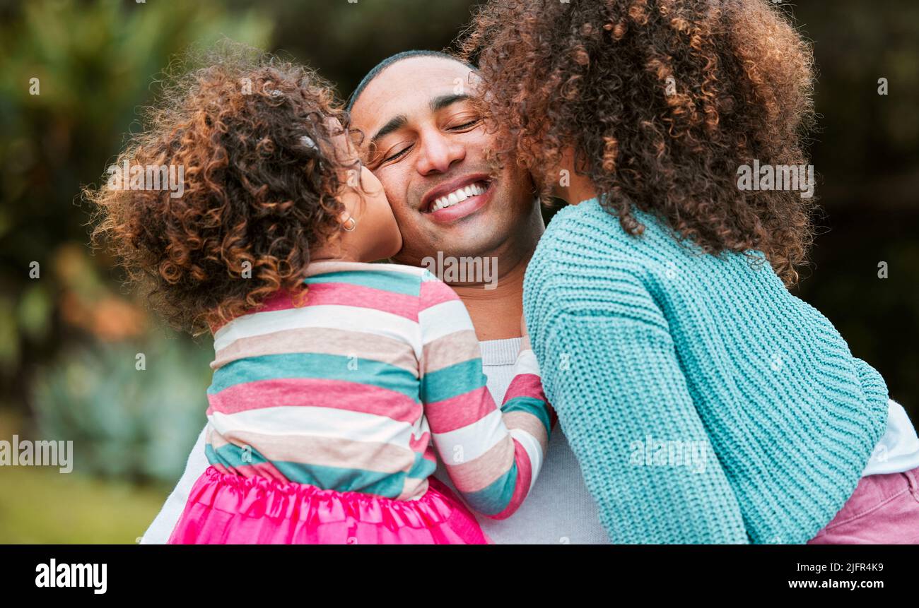 Being a dad is the best feeling in the world. Shot of two little girls kissing their father on his cheek. Stock Photo