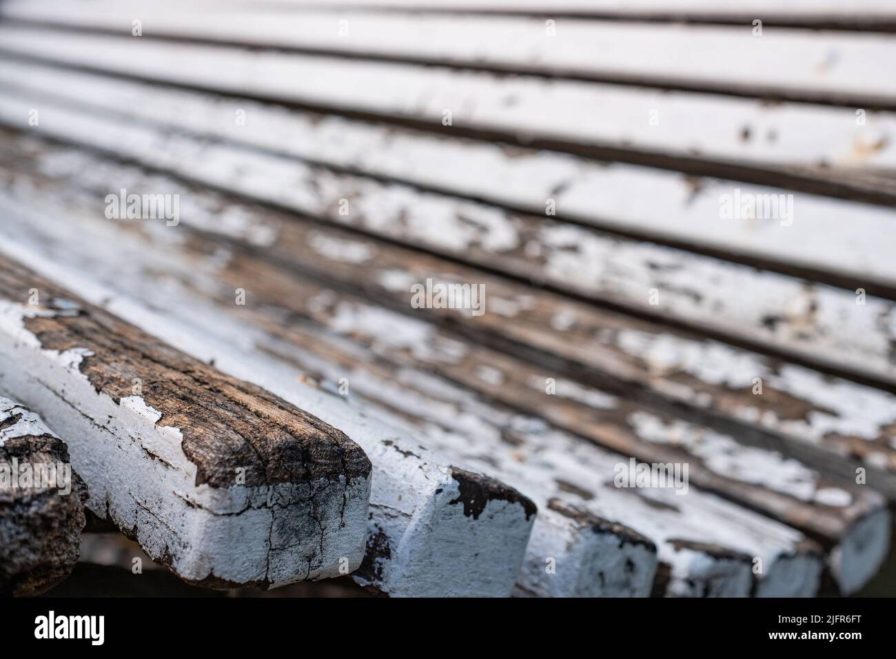 Close-up shot of an old weathered wooden bench. Close-up of the edge, details of peeling white paint and wood material. Side perspective view. Stock Photo