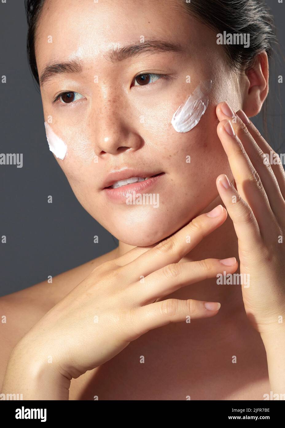 My skin stays hydrated everyday. Studio shot of a beautiful young woman posing with moisturiser on her face. Stock Photo