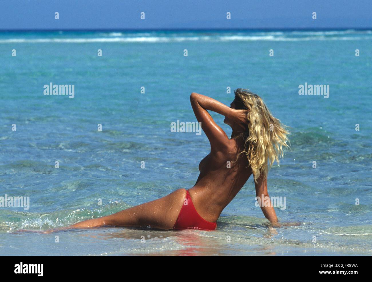 pretty blond hair young girl lay down on the beach back front camera  blue sky and seawater background topless silhouette Stock Photo