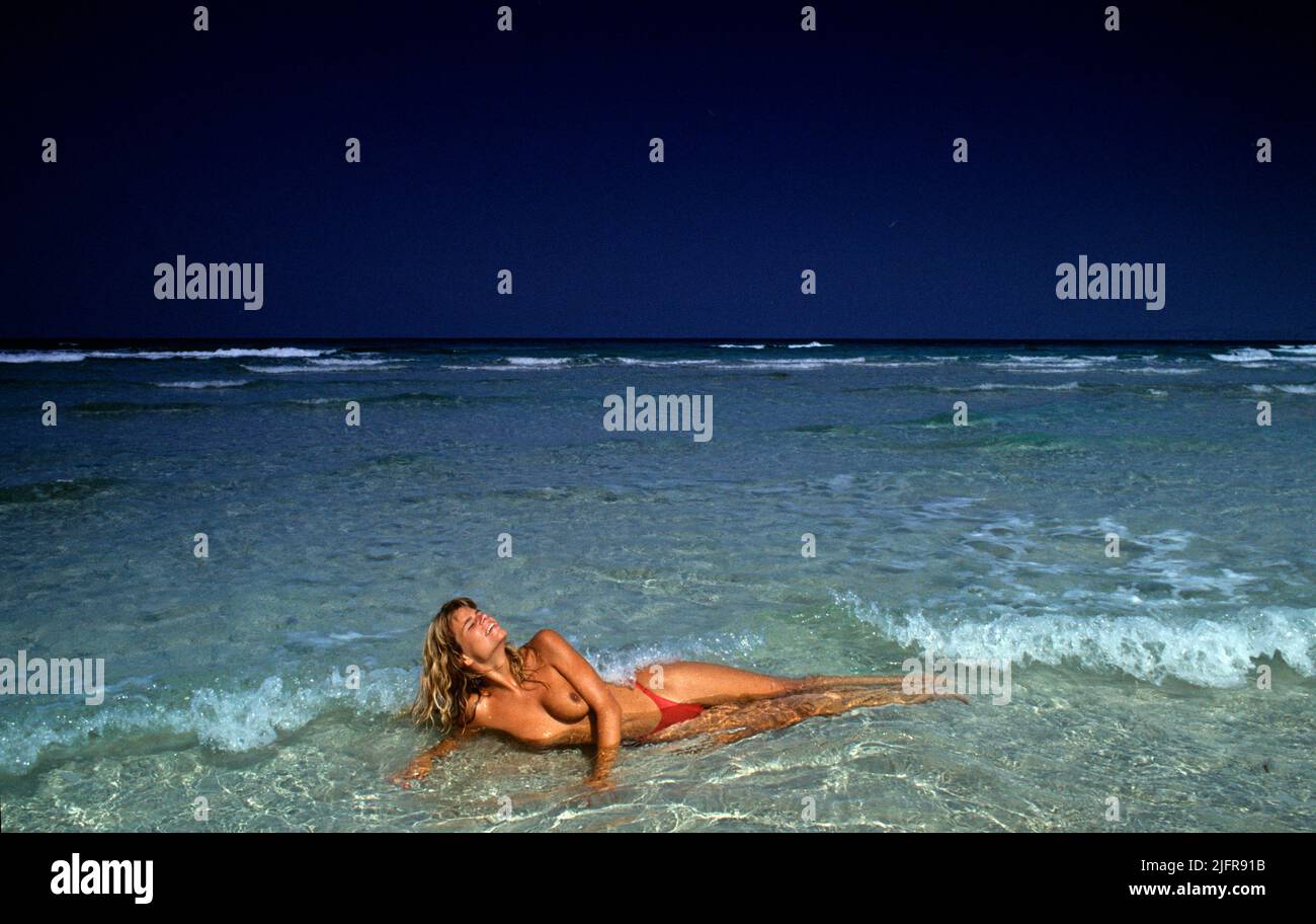 pretty young blond hair young woman lay down waves on the beach front camera topless seawater background Stock Photo