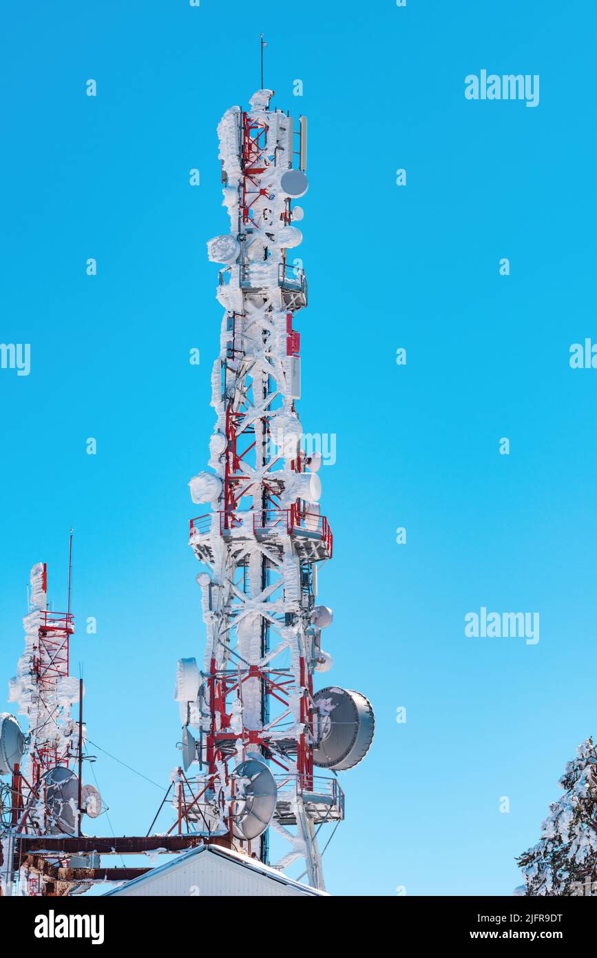 Telecommunication tower covered in snow against blue sky Stock Photo