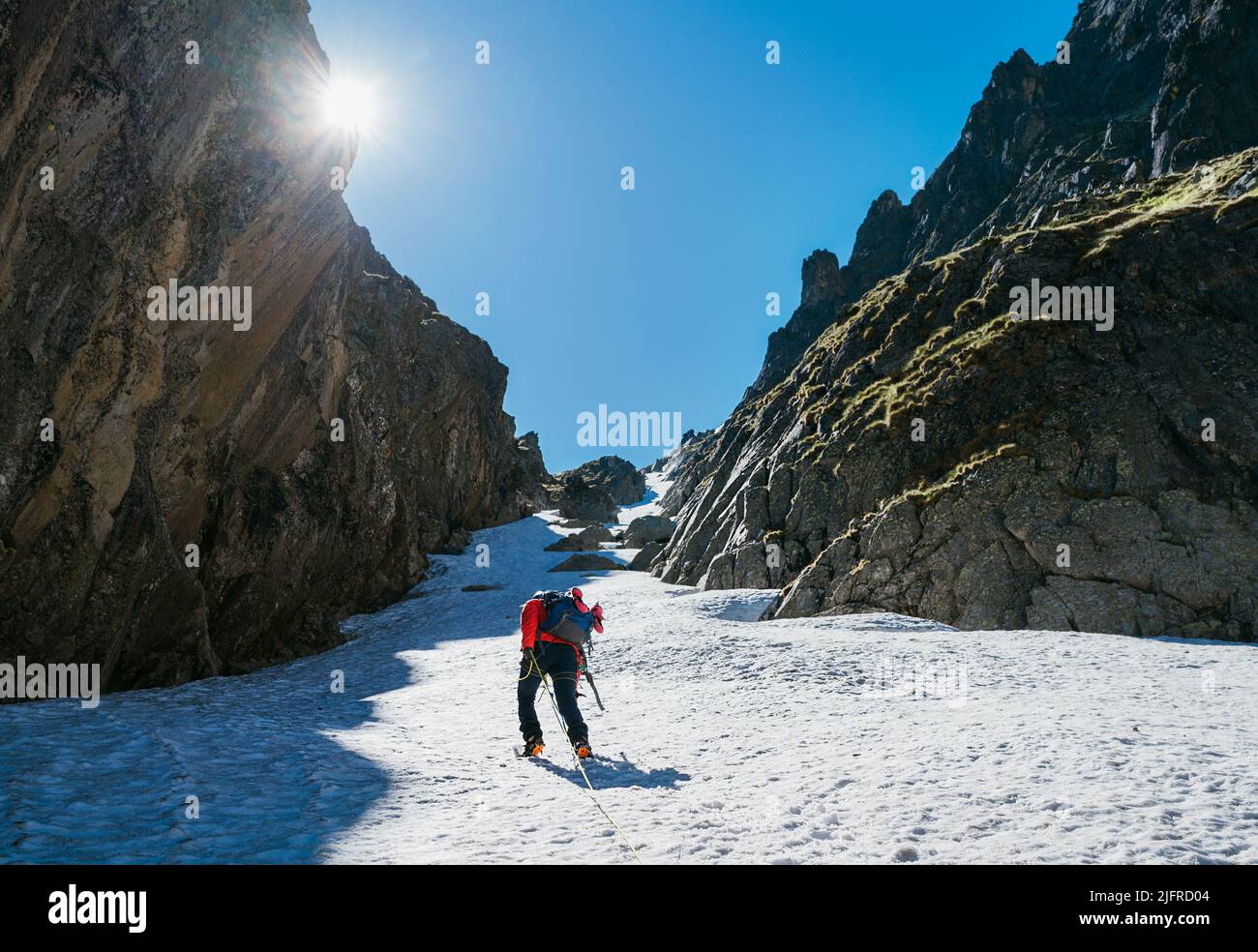 Team roping up woman with climbing axe dressed high altitude mountaineering clothes with backpack walking by snowy slope in the couloir with backlight Stock Photo