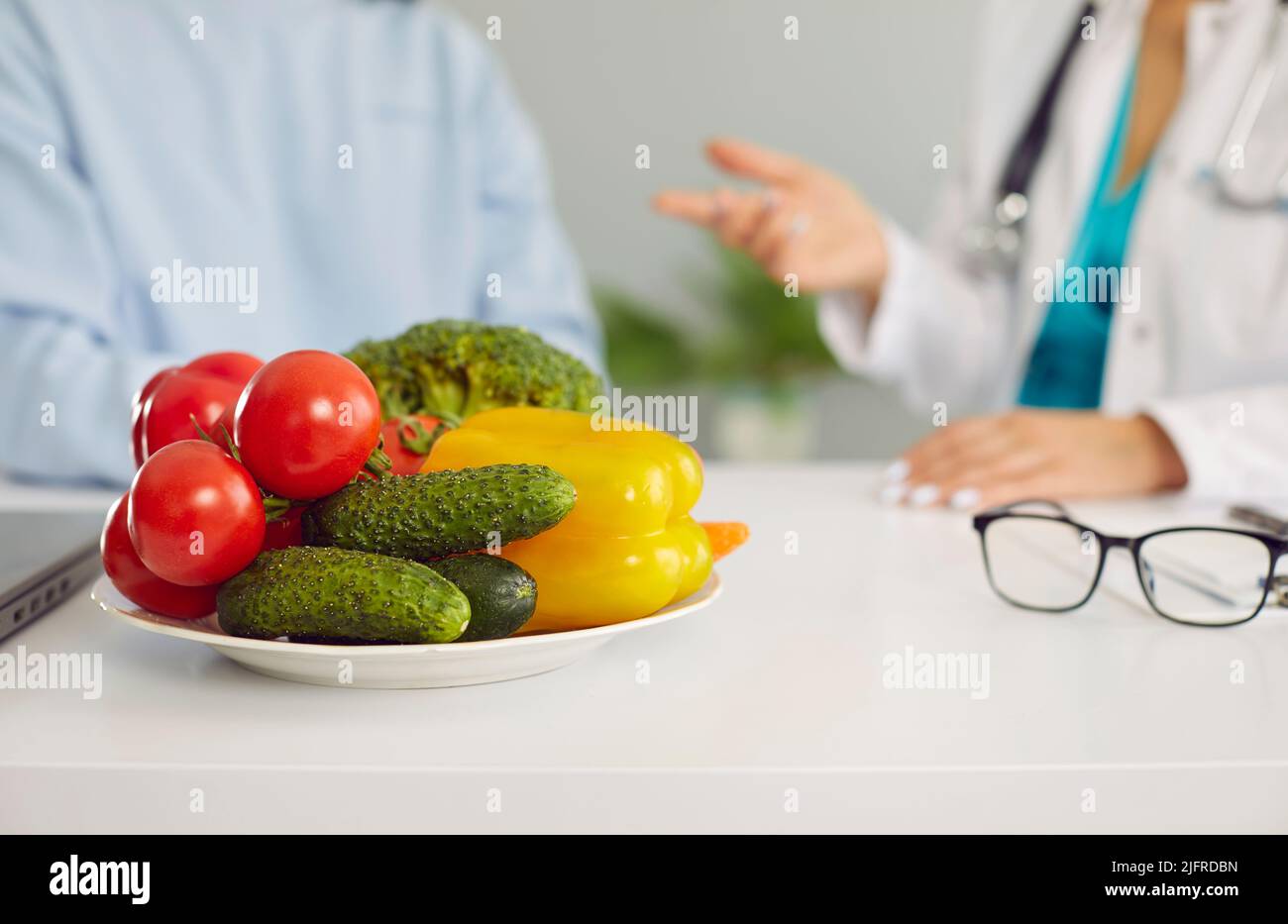 Vegetables on table of dietitian or nutritionist giving consultation to patient in background Stock Photo
