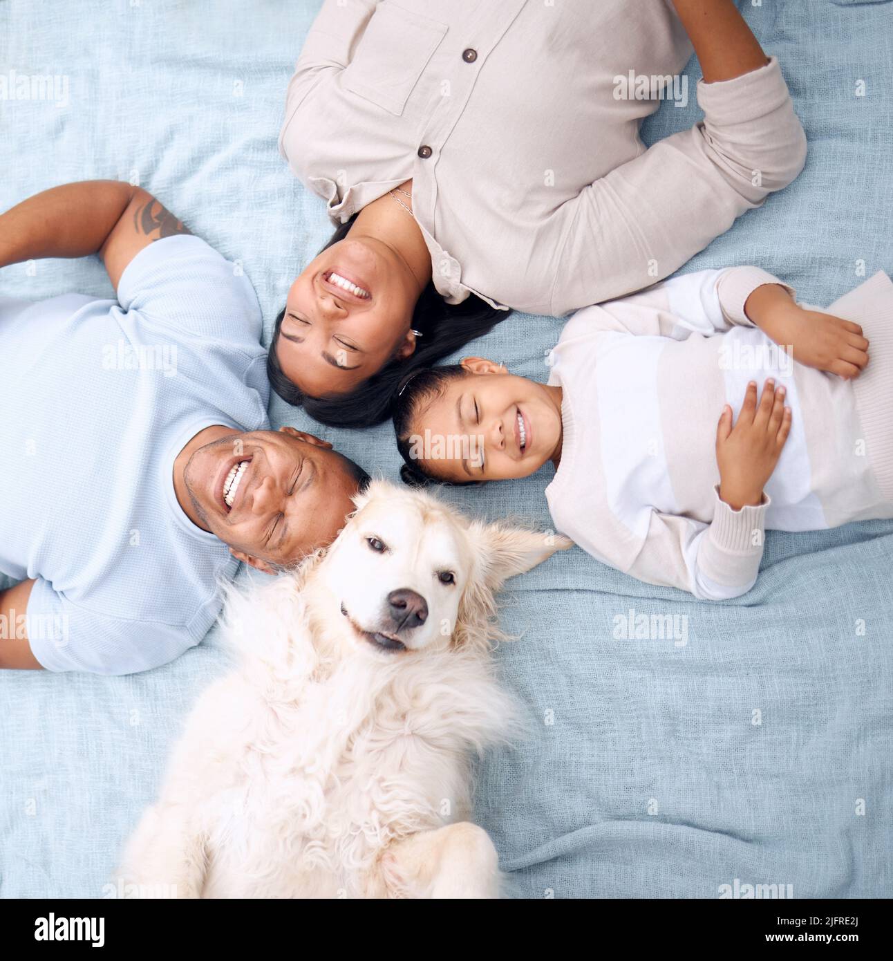 Our little family. Shot of a young family lying on the grass with their dog in their garden at home. Stock Photo