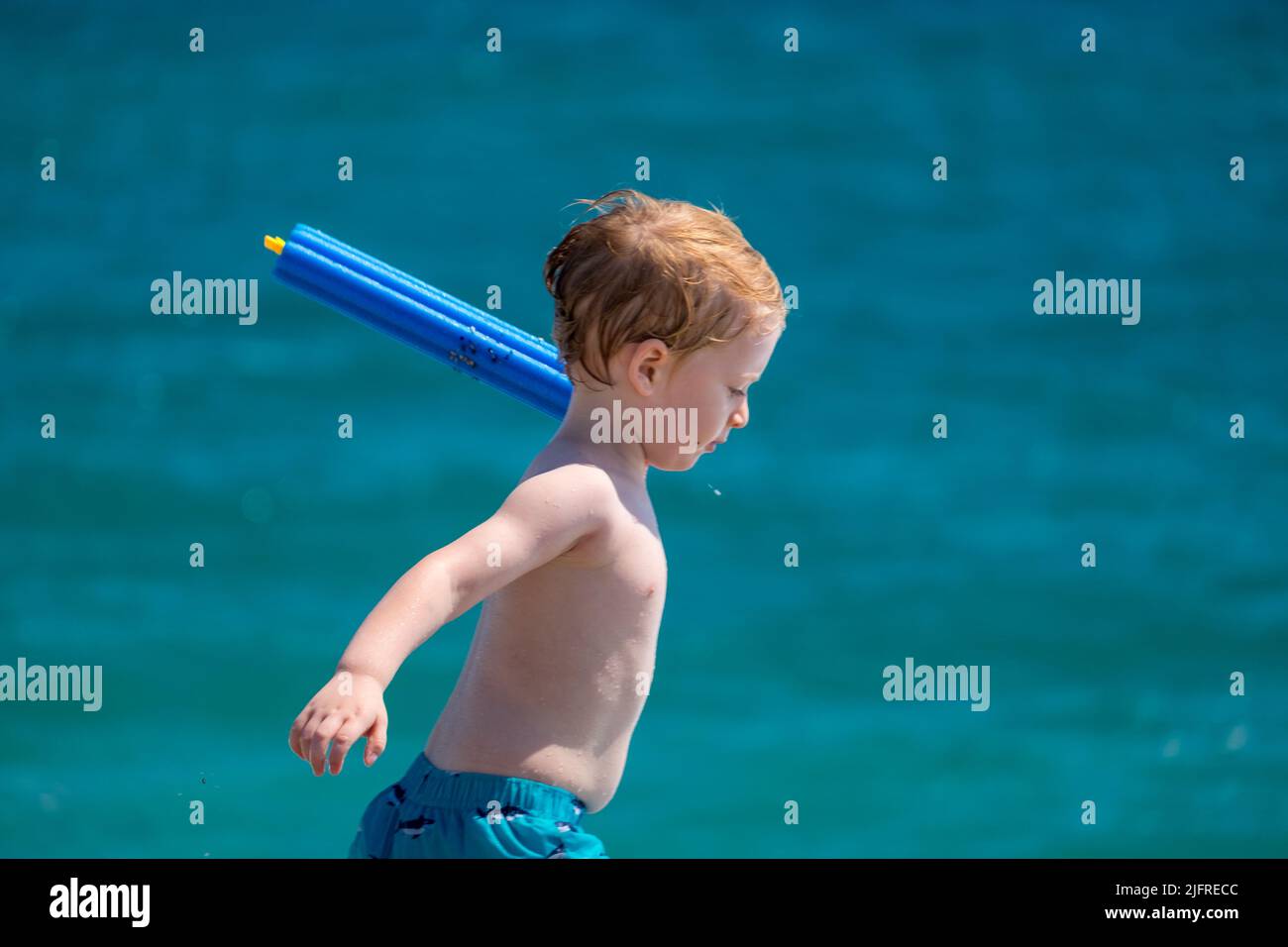 Cute little boy with blond hair playing with his water gun in the beach Stock Photo