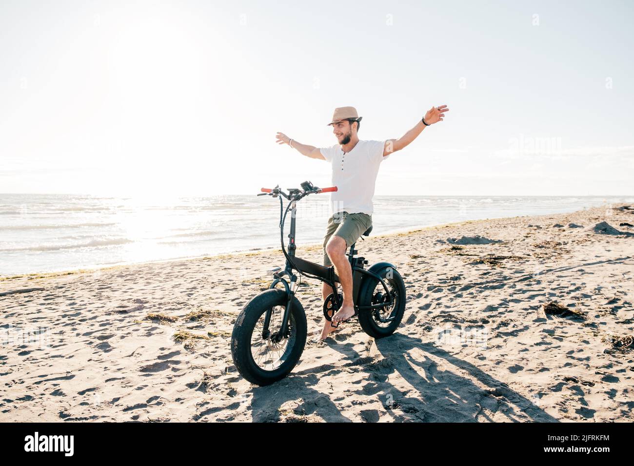 Young man on bicycle having fun with electric bike - carefree boy having fun and smiling on bicycle on the beach on a sunny day - freedom concept Stock Photo