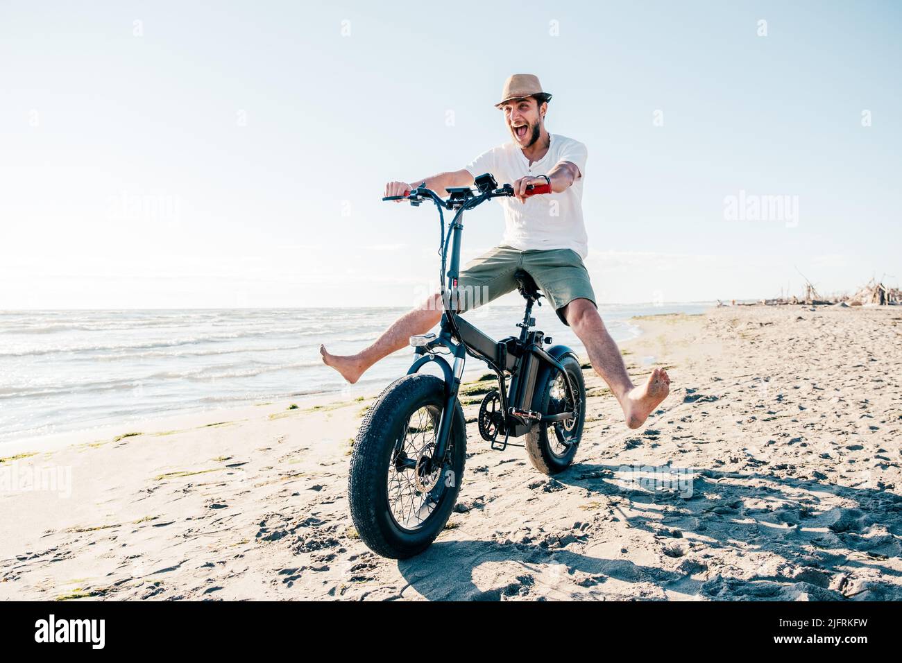 Young man on bicycle having fun with electric bike - carefree boy having fun and smiling on bicycle on the beach on a sunny day - freedom concept Stock Photo