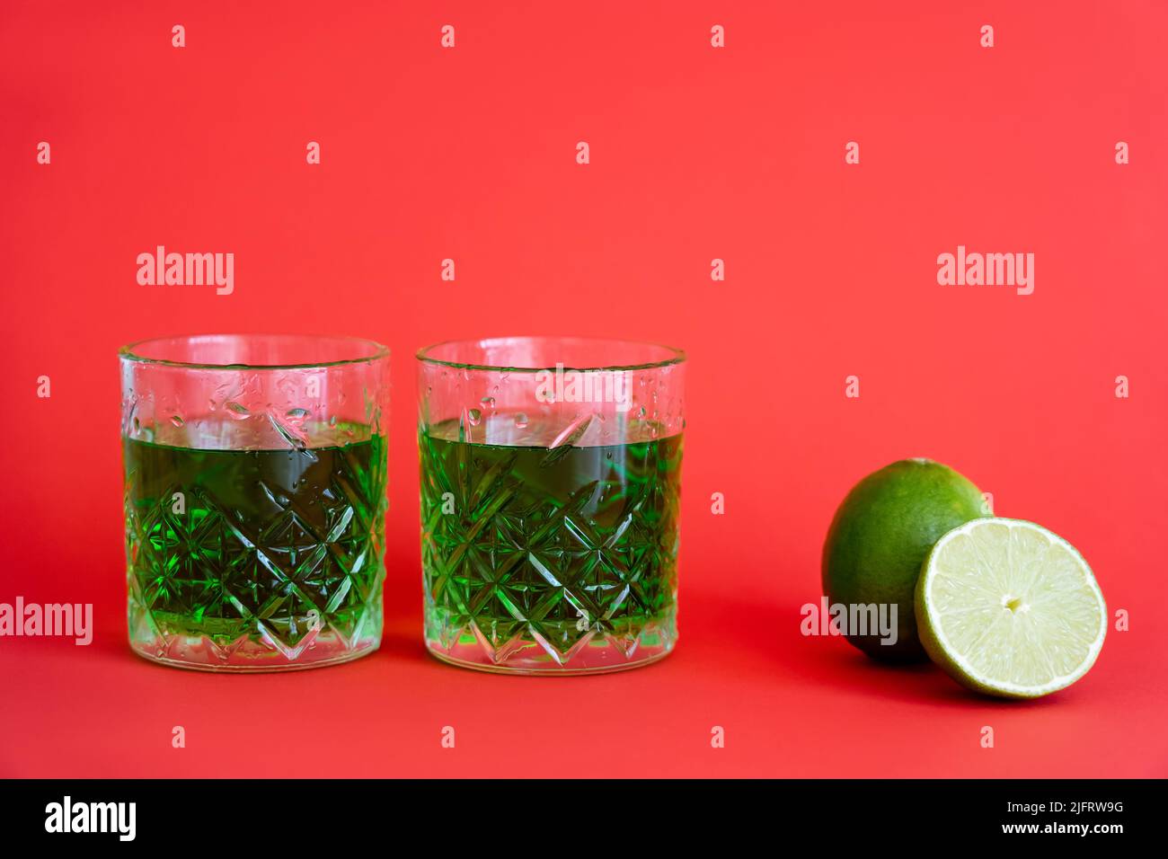 green alcohol drink in faceted glasses with water drops near limes on red Stock Photo