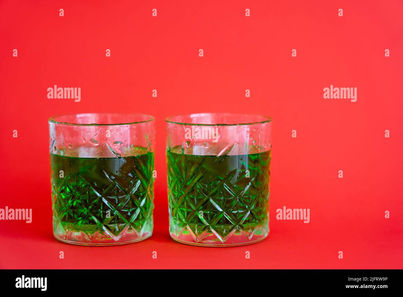 green alcohol drink in faceted glasses with water drops on red Stock Photo