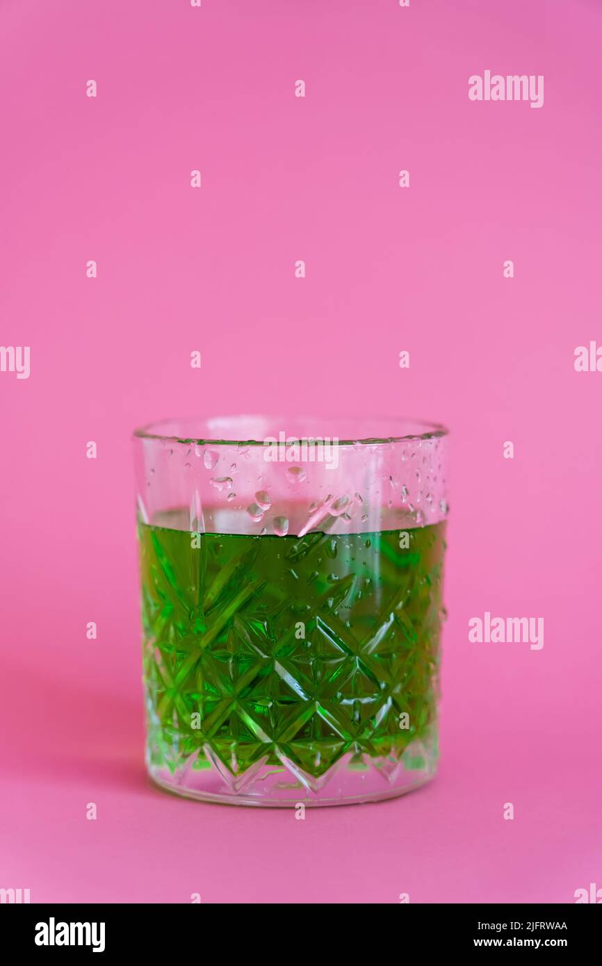 green alcohol drink in faceted glass with water drops on pink Stock Photo