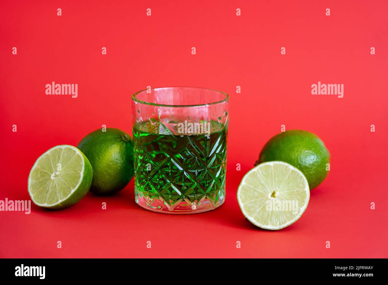 green alcohol drink in faceted glass near sour limes on red Stock Photo