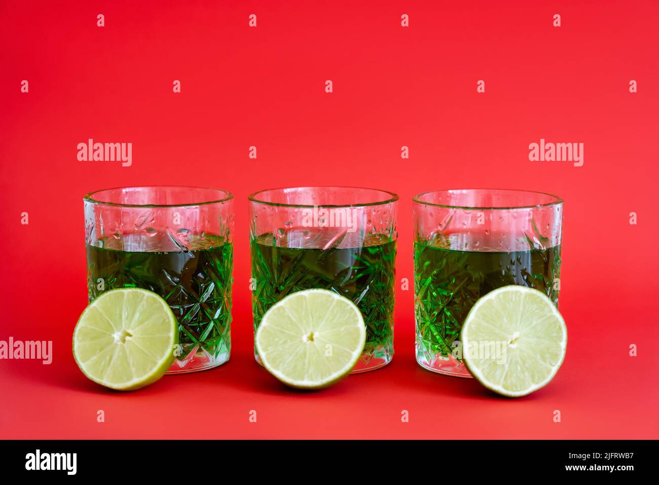 green alcohol drink in three faceted glasses with water drops and halves of limes on red Stock Photo