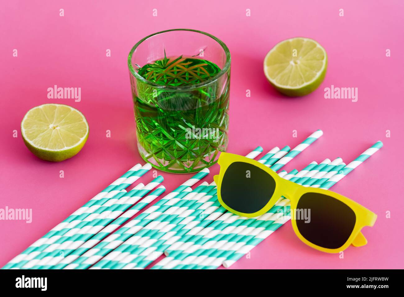 sunglasses and glass of green alcohol drink near striped paper straws and limes on pink Stock Photo