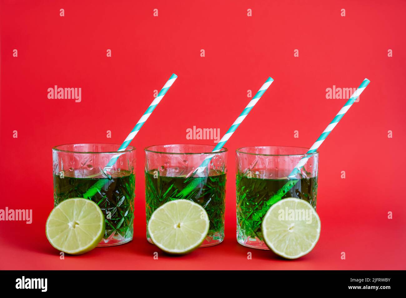 green alcohol drink in faceted glasses with straws and halves of limes on red Stock Photo