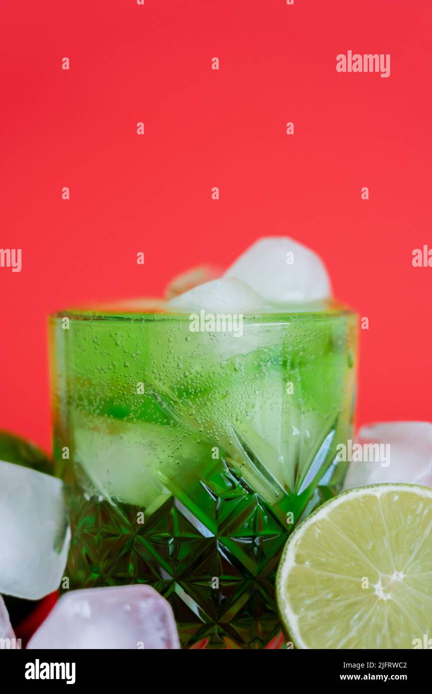 close up of frozen ice cubes in glass with sparkling green mojito and limes on red Stock Photo