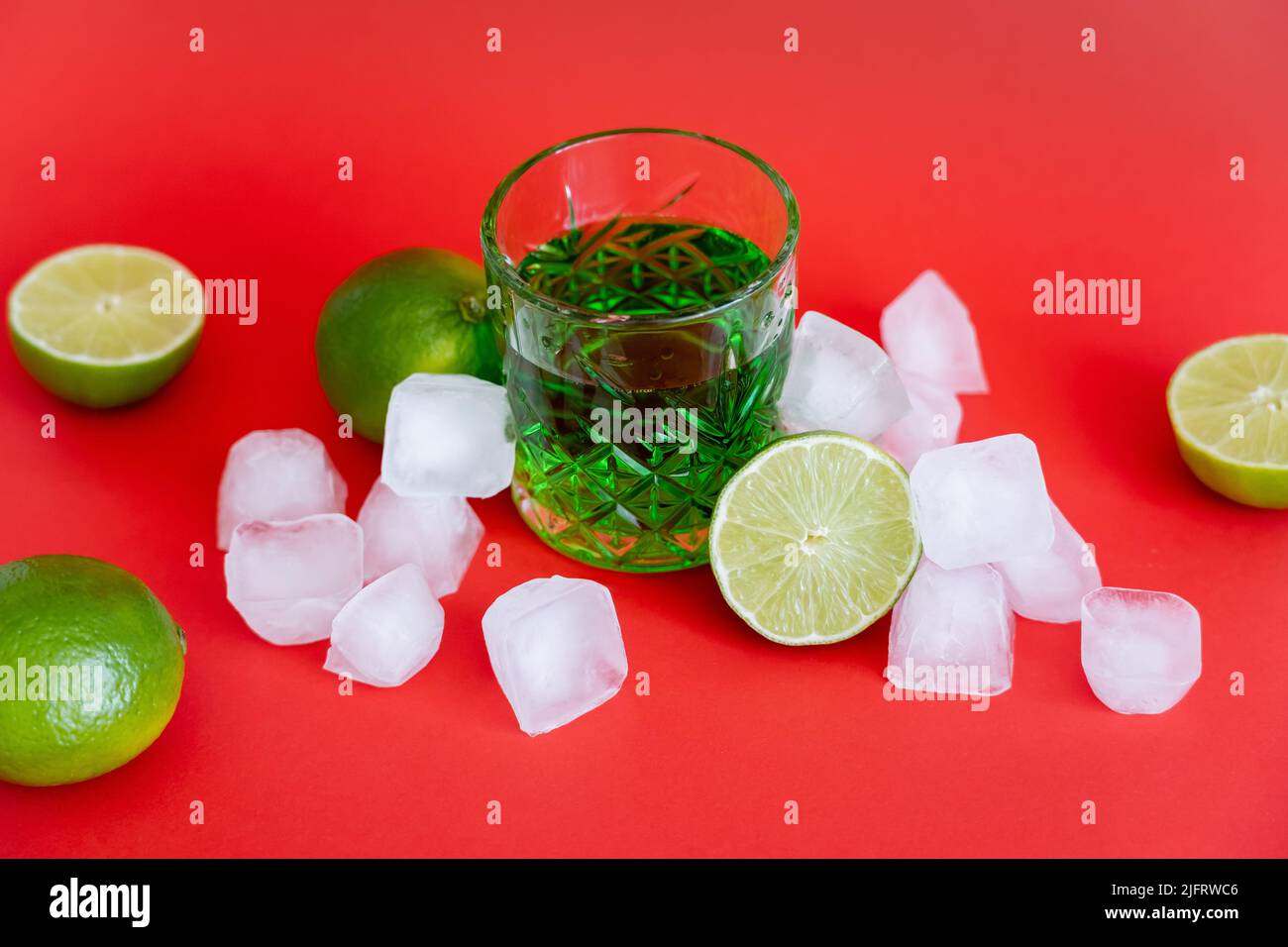 frozen ice cubes near glass with alcohol mojito and fresh limes on red Stock Photo