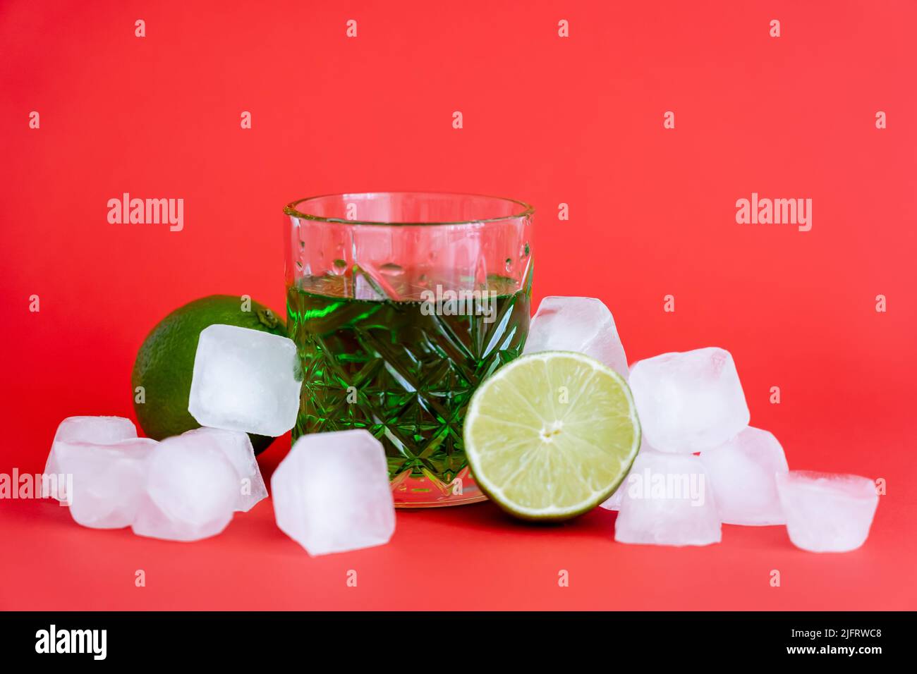 frozen ice cubes near glass with alcohol green drink and limes on red Stock Photo