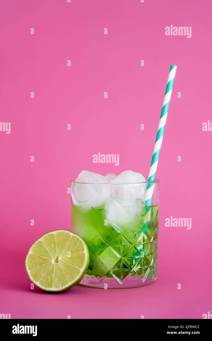 frozen ice cubes in glass with green mojito drink near sliced lime on pink Stock Photo