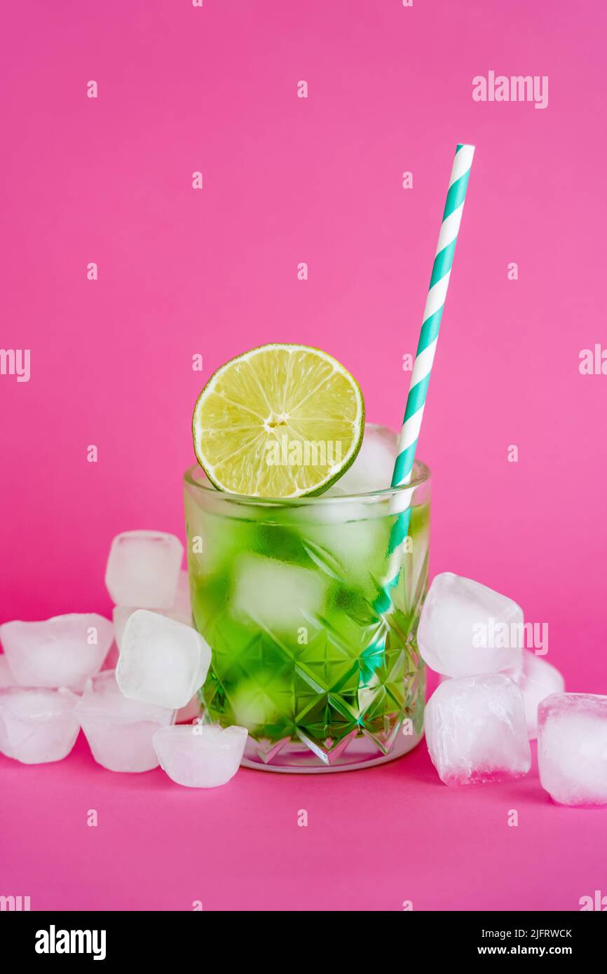 ice cubes in faceted glass with mojito drink and sliced lime on pink Stock Photo