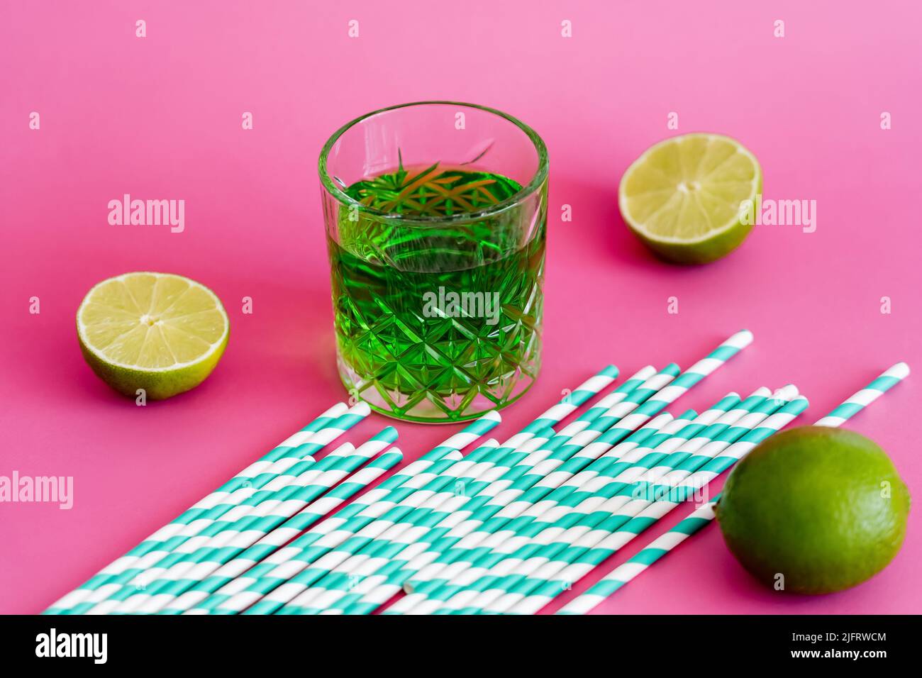 glass of green alcohol drink near striped paper straws on pink Stock Photo