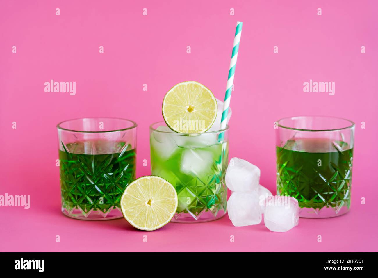 frozen ice cubes in glass with mojito near green beverages and limes on pink Stock Photo