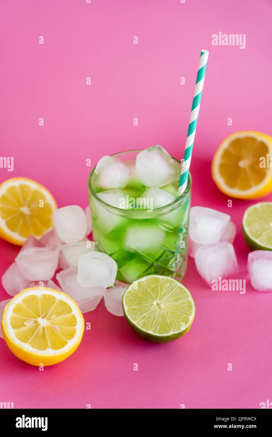 frozen ice cubes in glass with mojito drink and straw near citrus fruits on pink Stock Photo