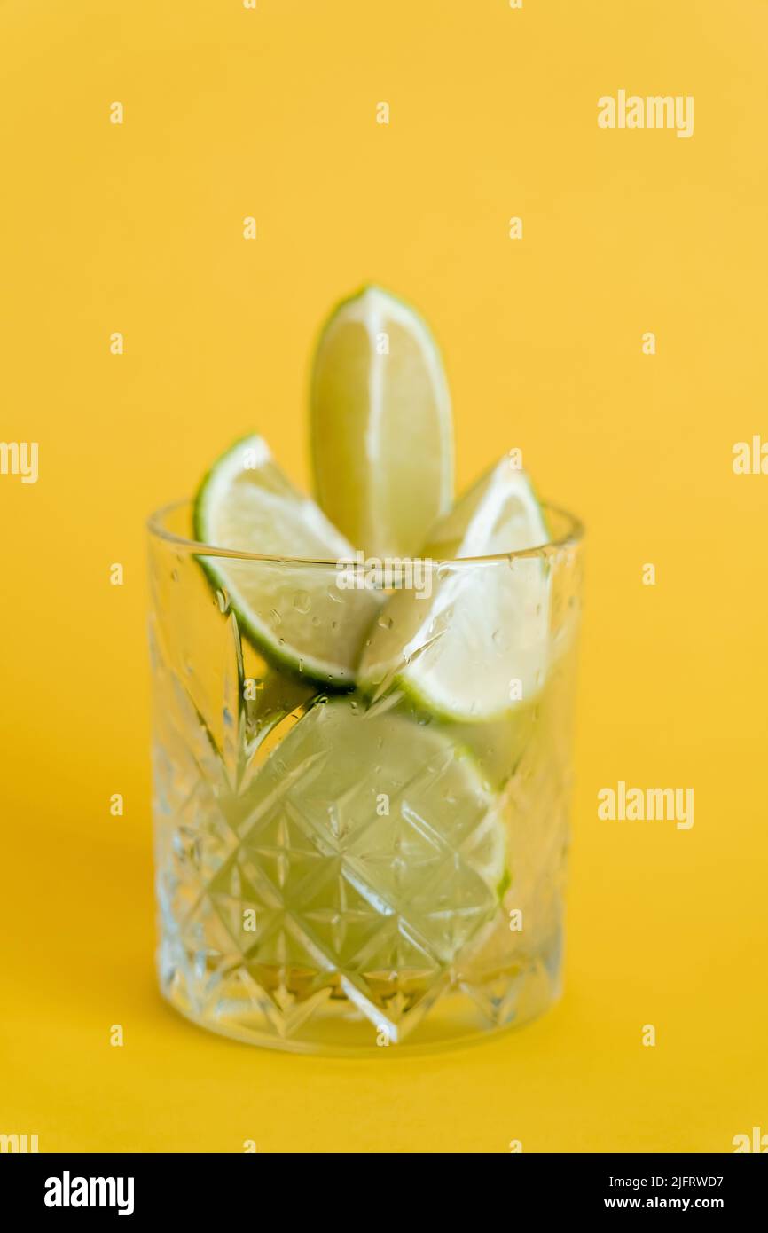 cool faceted glass with sliced fresh limes on yellow Stock Photo