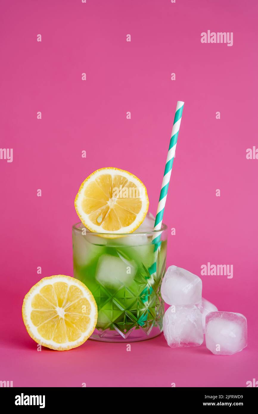 ice cubes in glass with mojito drink and straw near lemons on pink Stock Photo